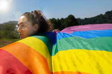 Woman wearing glasses holding rainbow waving flag outdoors. Lgtbiq concept.