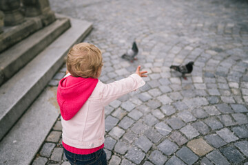Obraz na płótnie Canvas Little girl watching pigeons on square