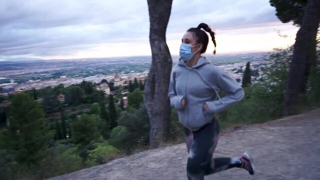 Young woman running outdoors wearing a coronavirus mask at sunset above the Alhambra in Granada. Healthy lifestyle, covid, active life and exercise.