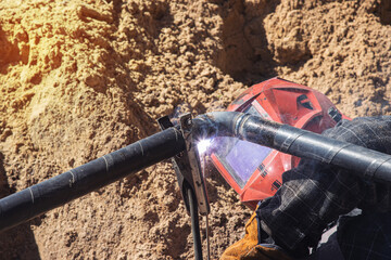 A professional welder in a protective shield does pipe welding using a machine. Close-up