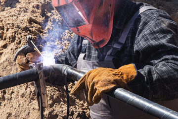 A worker wearing gloves and a protective shield welds pipes using a welding machine. The concept of welding