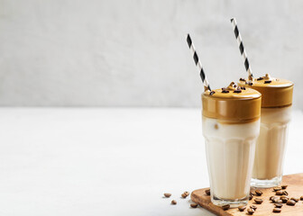Korean dalgona coffee with brown foam in tall glass close up on white background