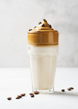 Korean dalgona coffee with brown foam in tall glass close up on white background
