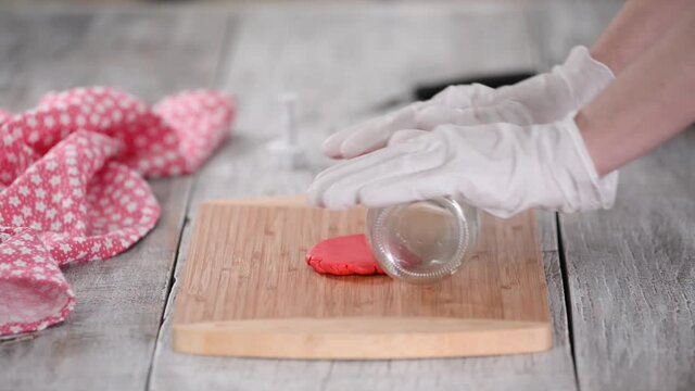 Woman rolling a sugar mastic with bottle on table.