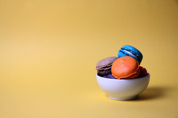 Macaroons of differrent colours in a bowl isolated on yellow background