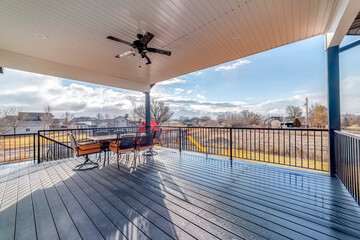Dining table chairs and ceiling fan with light on wooden deck with metal railing