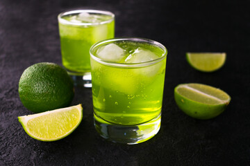 
Green drink with lime and ice on a black background.