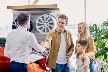 pleasant caucasian customers shake hand to responsive consultant of cars dealership, young family signed a purchase and sale document and received car keys