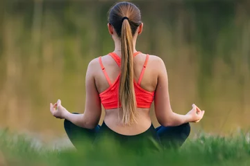 Fototapeten Lotusblume Back view of young girl doing yoga outdoor near lake  © Ivan