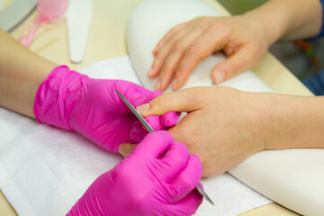 Closeup shot of a woman in a nail salon receiving a manicure by a beautician with nail file. Woman getting nail manicure.