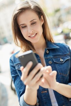 Outdoor portrait of young woman using mobilephone, smiling.