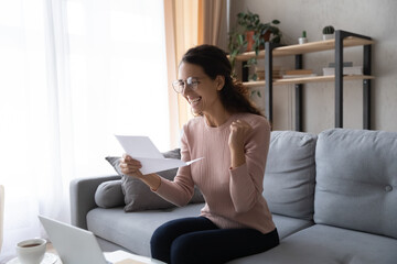 Excited woman wearing glasses reading letter with good news, celebrating success, showing yes...