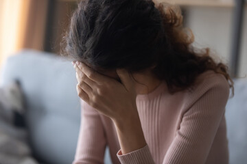 Fototapeta premium Close up frustrated depressed woman touching forehead, feeling headache, sitting on couch alone, lost in thoughts, unhappy sad girl suffering from break up or divorce, unexpected pregnancy