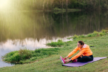 Woman doing exercise on grass near lake. Stretching, meditation,