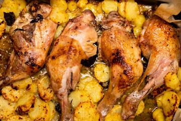 Roasted chicken legs in a pan, cooked and garnished with sliced potatoes. Top view, close-up, full frame.