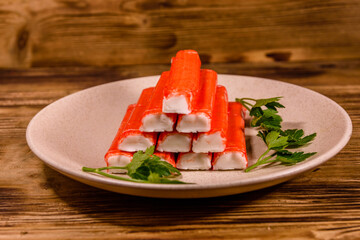 Ceramic plate with pile of crab sticks and parsley twig on a wooden table