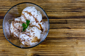 Glass bowl with ice cream balls, mint leaf and chocolate topping on a wooden table. Top view