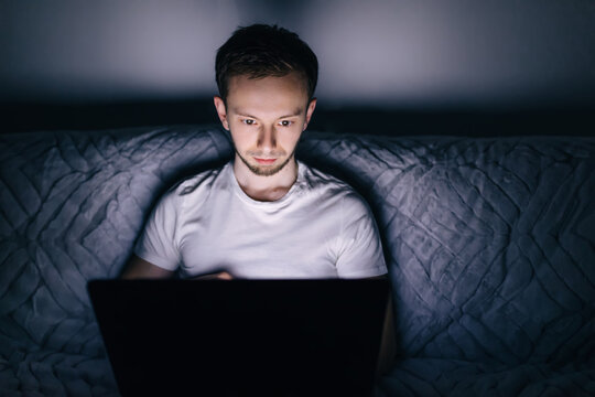 Young Man Sitting On Sofa At Home, Holding Laptop Computer On La