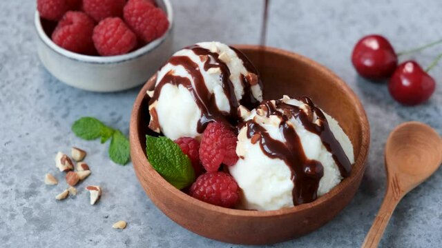 Chocolate pouring on vanolla ice cream scoops. Serving homemade vegetarian ice cream in a bowl with berries, nuts and chocolate syrup