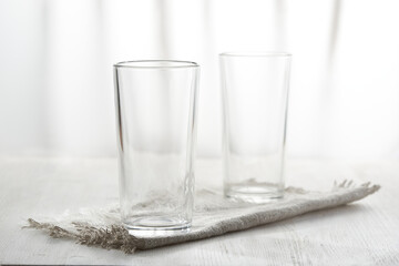 Two empty glasses on linen napkin on white background in blur.