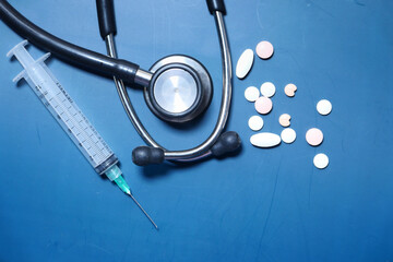 pills, stethoscope and syringe on blue background 