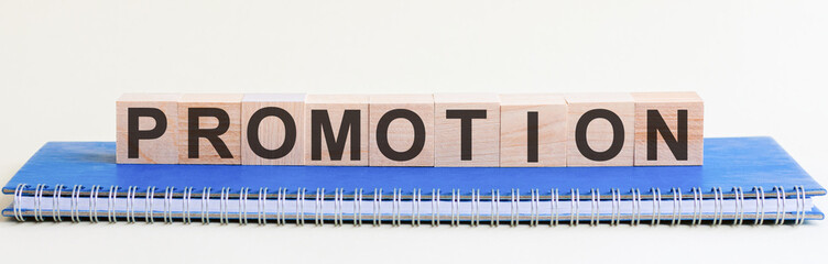 Promotion - a word made of wooden blocks with black letters, a row of blocks is located on a blue Notepad. White background, front view. Promotion code, promo code concept.