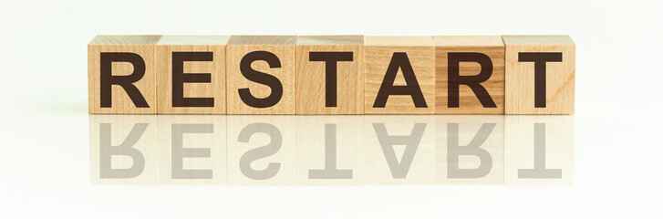 Wooden Blocks with the text: Restart. The text is written in black letters and is reflected in the mirror surface of the table. New business relaunch startup concept.