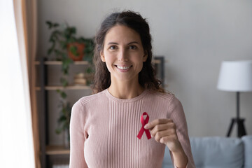 Head shot portrait smiling young woman holding awareness red ribbon, symbol of fight against AID, HIV, cancer, drugs addiction, supporting people with disease, regular checkup promotion