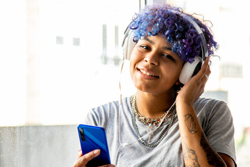 young woman afro american with headphones and mobile phone at the window