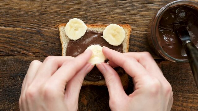 Healthy funny food art breakfast toast for kids. Making teddy bear toast with chocolate nut butter, banana and blueberries. Breakfast or school lunch for kids