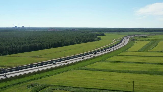 Asphalt ringroad. Speedway with cars through green field near forest. Aerial view from drone