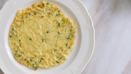 Top view of egg omelette with spring onion, served on a plate.