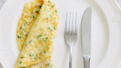 A folded egg omelette served on a plate, with knife and fork at the side.