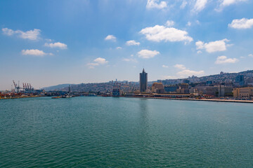 Fototapeta premium Haifa Port in Israel, featuring calm blue waters, industrial cranes, cargo ships, and a city skyline in the background. The harbor is active with maritime operations, while the sky is partly cloudy