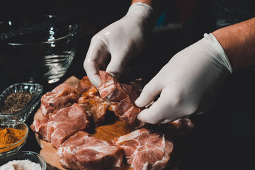 Marinating raw pork for cooking kebabs and ham. The chef of the restaurant in gloves treats the meat with basil and curry spices.