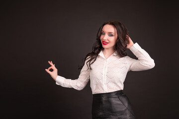 Girl business with red lips smiles and shows approval sign isolated against black background