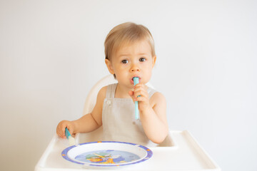 Blond baby sitting in the high chair with striped overalls