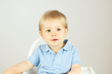 Blond baby with blue polo shirt sitting and smiling