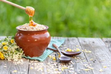 Oatmeal porridge in a pot with honey. Natural rustic porridge in the fresh air.