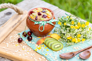 Oatmeal in a clay pot with cherries and kiwis on a wooden tray. Country Breakfast in the nature.