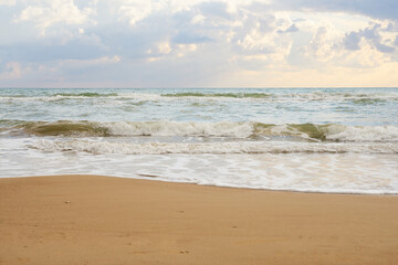 Sandy beach on a sunset with reflection on wet sand and waves with foam. Copy space.