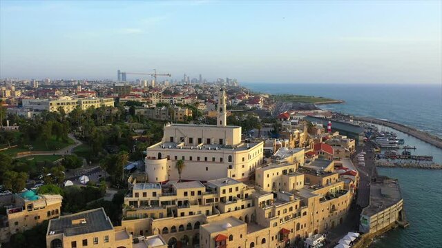 Aerial panning shot of church amidst buildings in city near sea, drone flying over cityscape against sky during sunset - Jaffa, Israel
