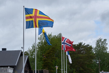 The flag of Åland and flags of nordic countries against a cloudy sky. 