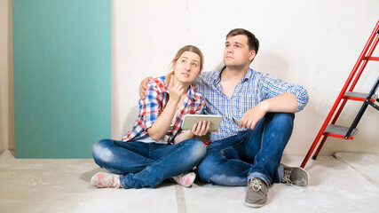 Smiling young couple choosing design for their new house on tablet computer
