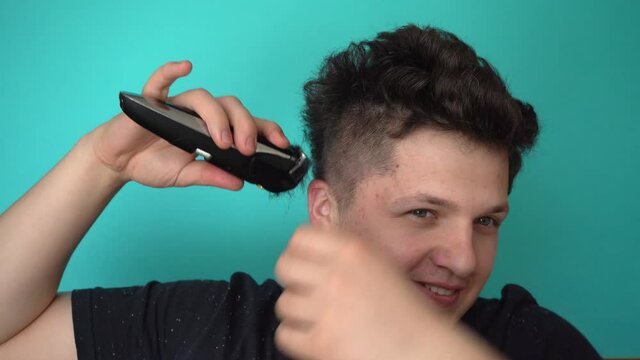 Brunette cuts himself with electric trimer. Smiles to himself Blue background 4K