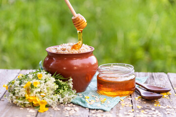 Honey drips from a spoon onto oatmeal porridge in an earthen pot. Rustic Breakfast with oatmeal and...