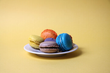 Macaroons of differrent colours on a saucer isolated on yellow background