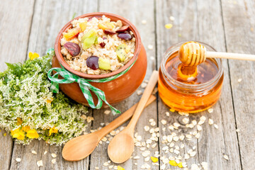 Fruit oatmeal porridge with honey in a clay pot on a wooden surface. Village Breakfast.