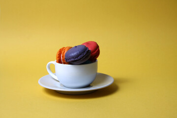 Macaroons of differrent colours in a tea cup isolated on yellow background