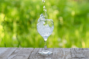Water is poured into a glass against a background of green greenery.